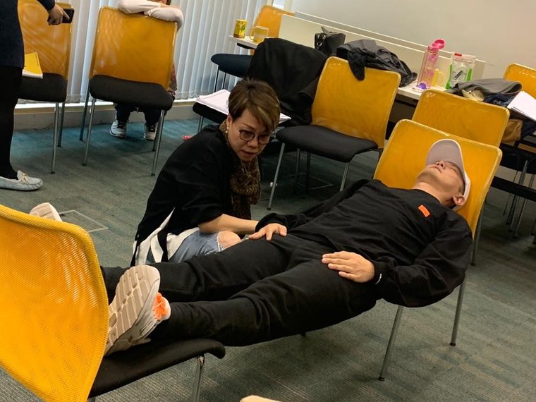 A trainer kneeling beside a participant who is lying back on a chair during a hypnotherapy session