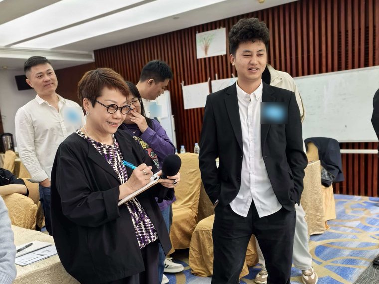 A trainer taking notes and listening while a participant presents his drawing