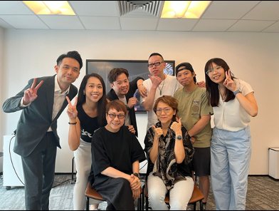 A group of seven people smiling and posing with peace signs in a meeting room