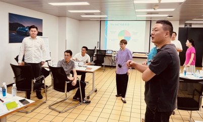 Participants at a training session standing and sitting around desks while a chart is shown on a screen