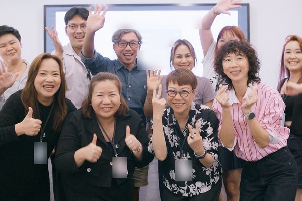 A group of smiling workshop participants waving and giving thumbs up and finger hearts